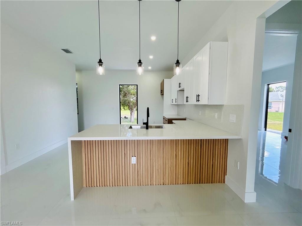 Kitchen featuring a waterfall-edge island with wood-finish paneling, white shaker-style cabinetry, and pendant lighting