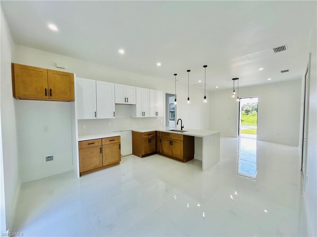 Open-concept kitchen featuring two-tone cabinetry, a central island with an undermount sink, pendant lighting, and recessed ceiling lights