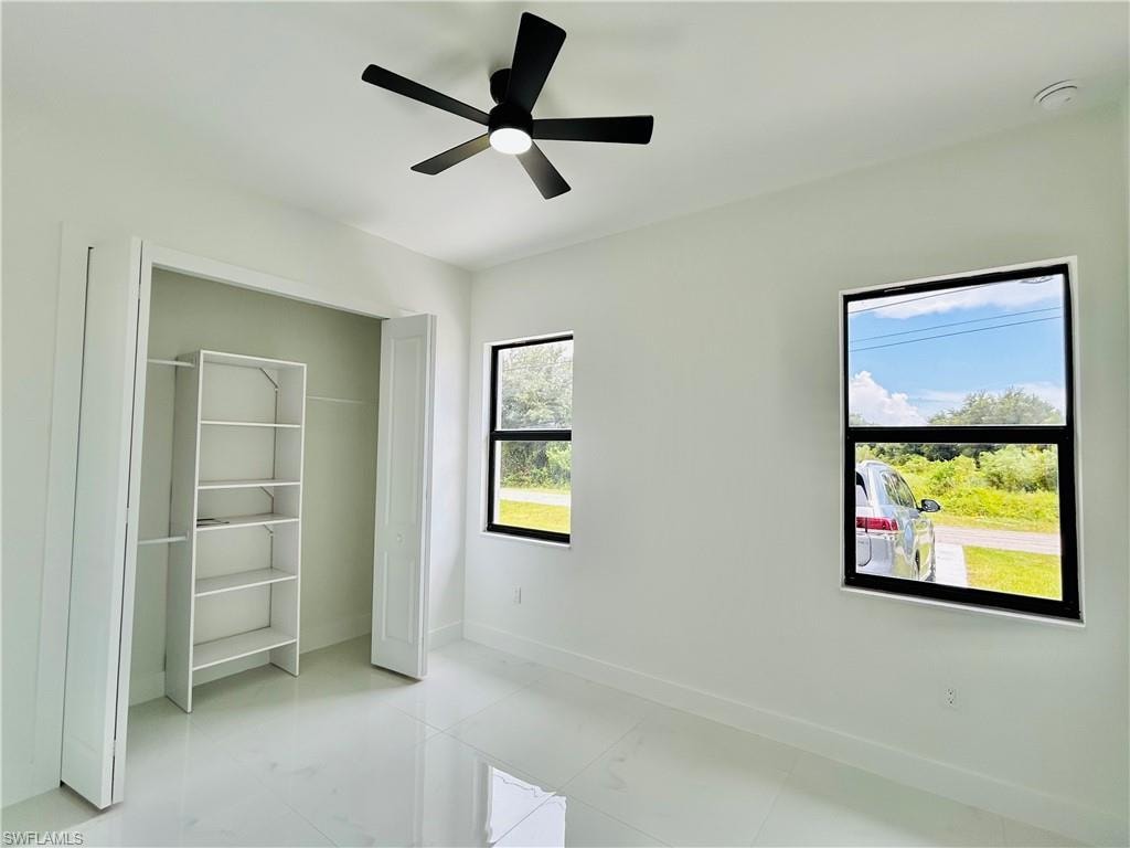 White tile flooring, bright white walls, modern black ceiling fan, dual windows with black frames, and built-in closet shelving