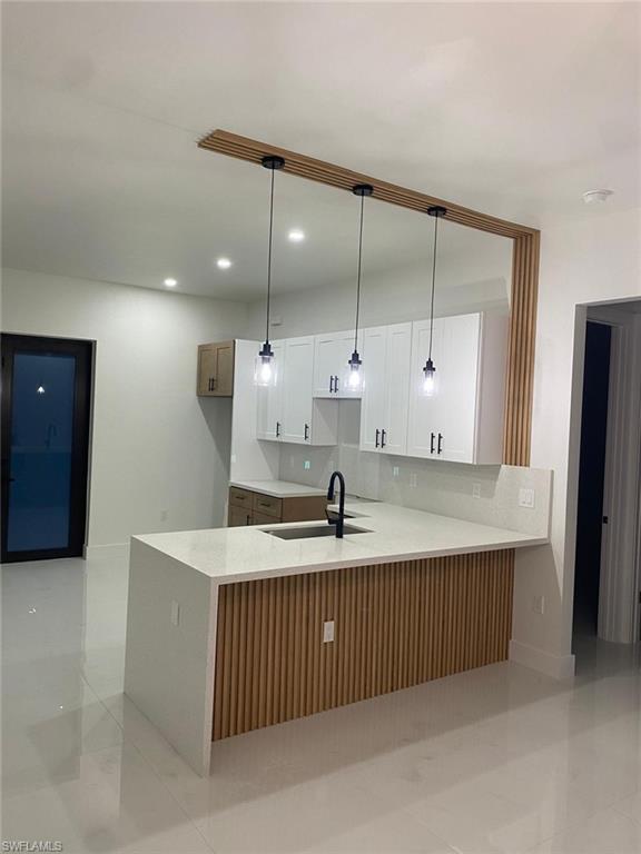Kitchen featuring a waterfall island with wood-finish paneling, white shaker-style cabinetry, and pendant lighting
