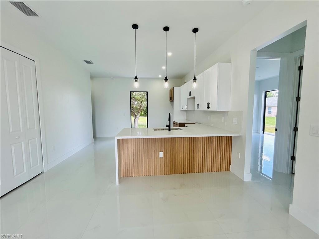 White tile flooring, white shaker cabinetry, pendant lighting, kitchen island with wood-finish paneling, and a black faucet