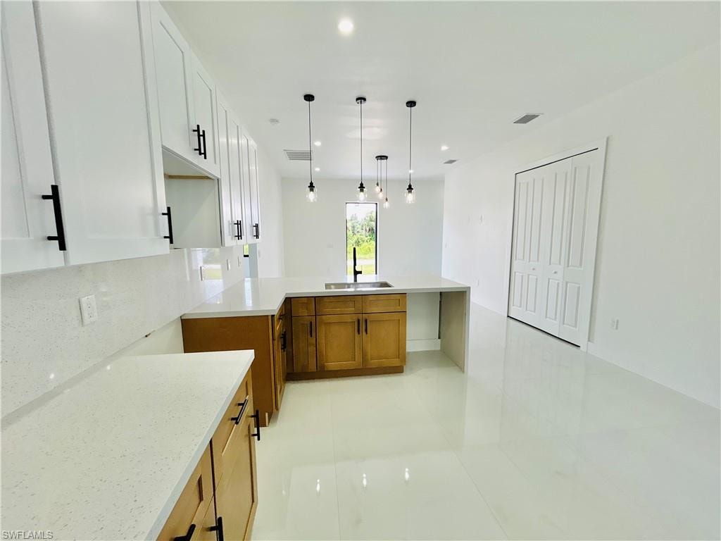 White shaker cabinetry, wood-tone base cabinetry, light-toned countertops, contemporary pendant lighting, and white tile flooring
