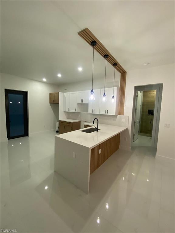 Kitchen featuring a waterfall-edge island, integrated sink with matte black faucet, and pendant lighting