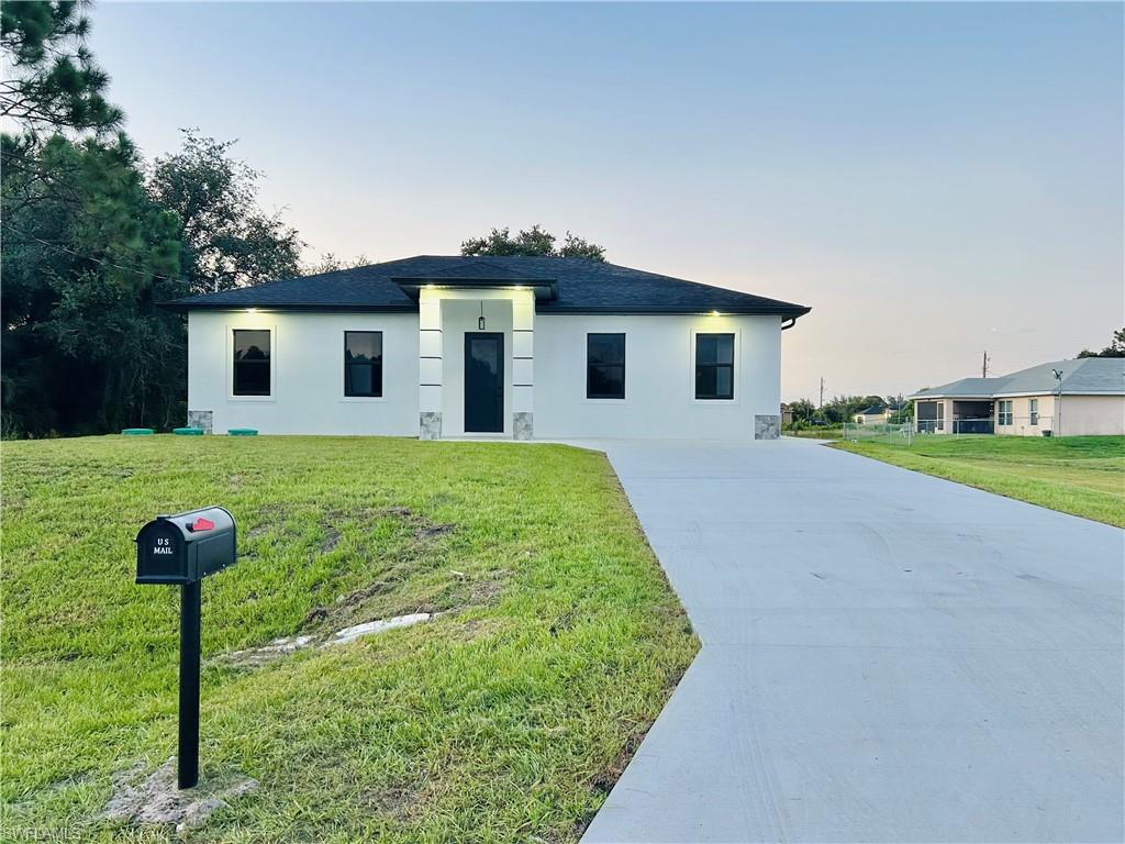 White stucco exterior with dark-framed windows, black shingle roof, and a concrete driveway