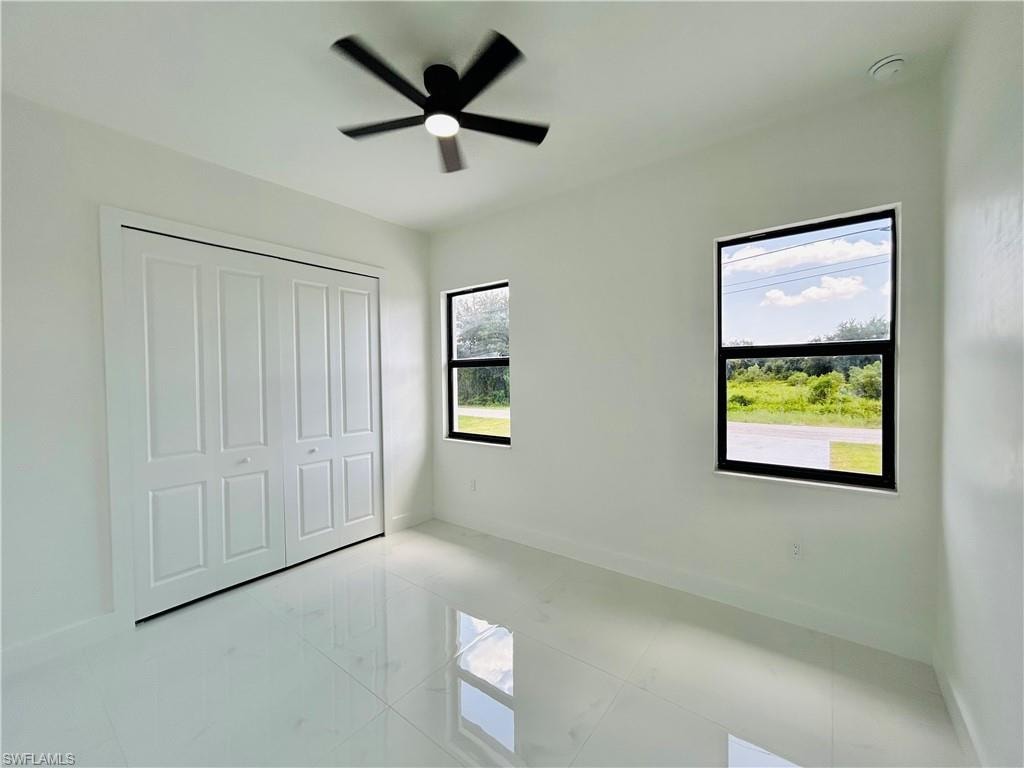 White tiled flooring with a polished finish, white walls, and a black ceiling fan