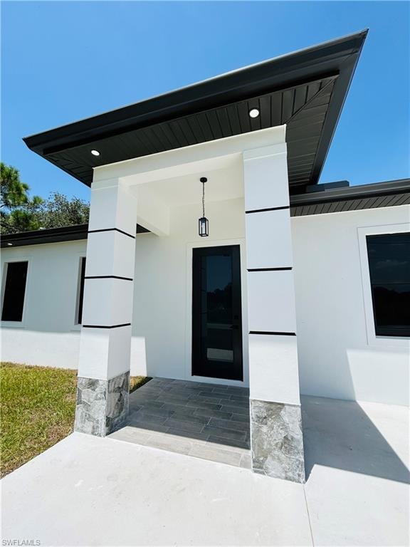 Sleek black roofline with recessed lighting, modern black entry door with glass panel, white exterior walls with black accent banding, and stone veneer column bases