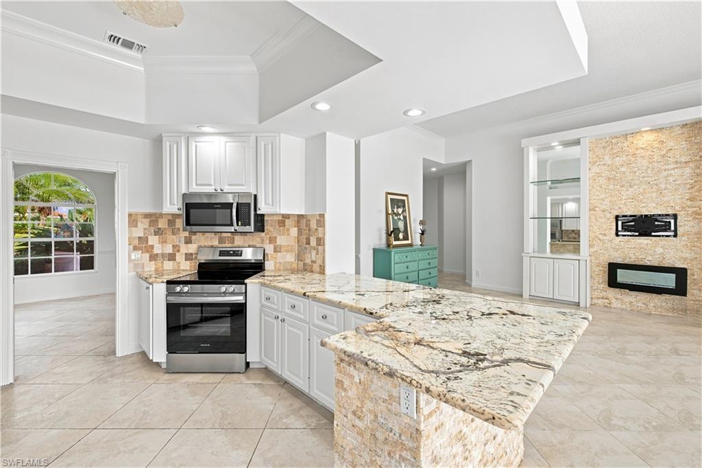 Kitchen featuring an expansive granite-top island, stainless steel appliances, white cabinetry, and a tile backsplash