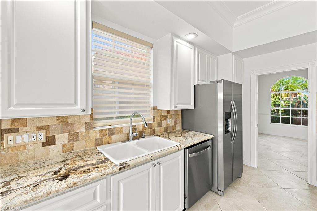 White cabinetry, stone tile backsplash, patterned countertops, stainless steel appliances, and arched doorway
