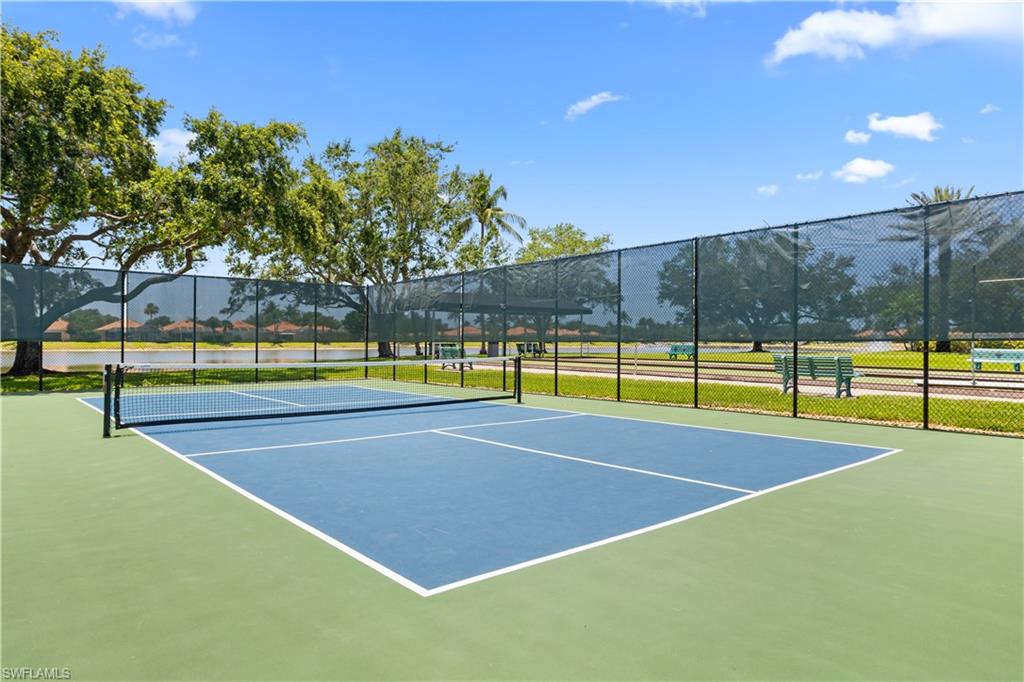 Pickleball court with a blue playing surface and green surrounding area, enclosed by a perimeter fence