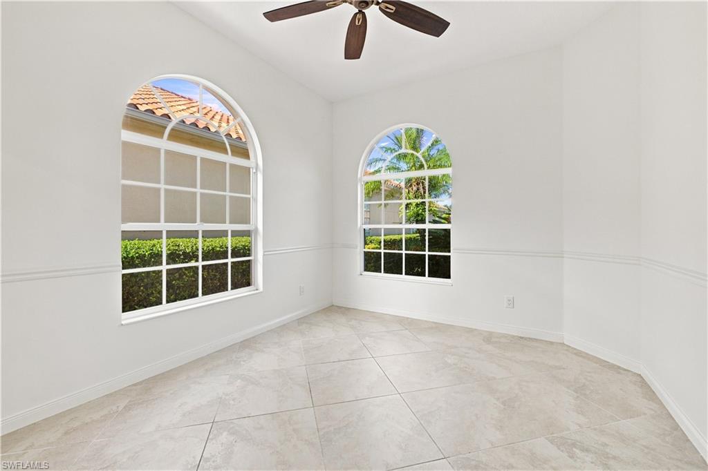 Arched windows with grid patterns, ceiling fan with dark wood-finish blades, light-toned tile flooring, and decorative wall molding