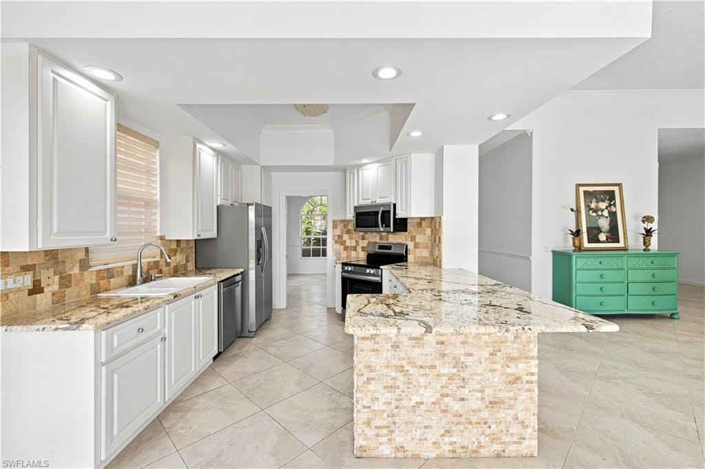 Kitchen featuring white cabinetry, stone tile flooring, stainless steel appliances, a tile backsplash, and an island with a stone countertop