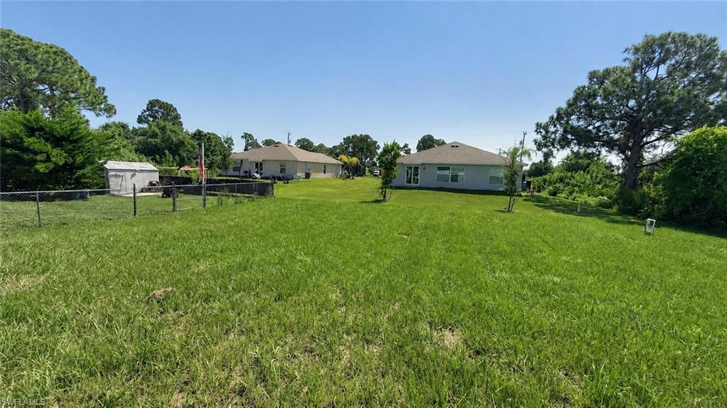 Expansive green space with a chain-link fence, mature trees, and a storage shed