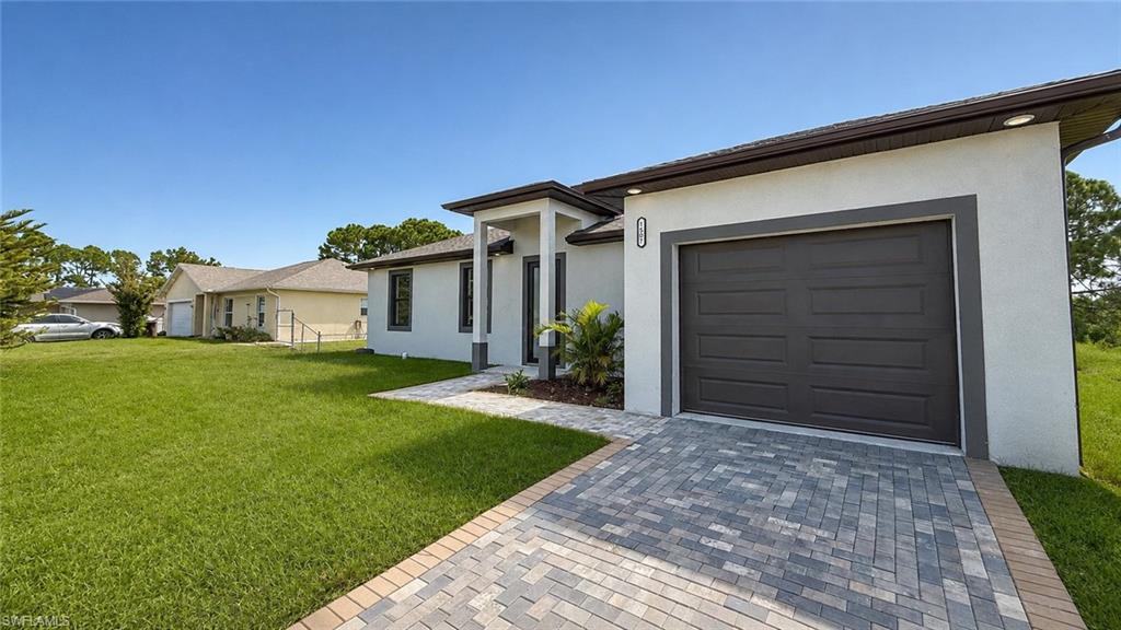 Modern residence featuring a spacious paver driveway, oversized two-car garage with dark finish door, crisp white exterior with contemporary trim detailing, and manicured lawn with mature landscaping framing the property