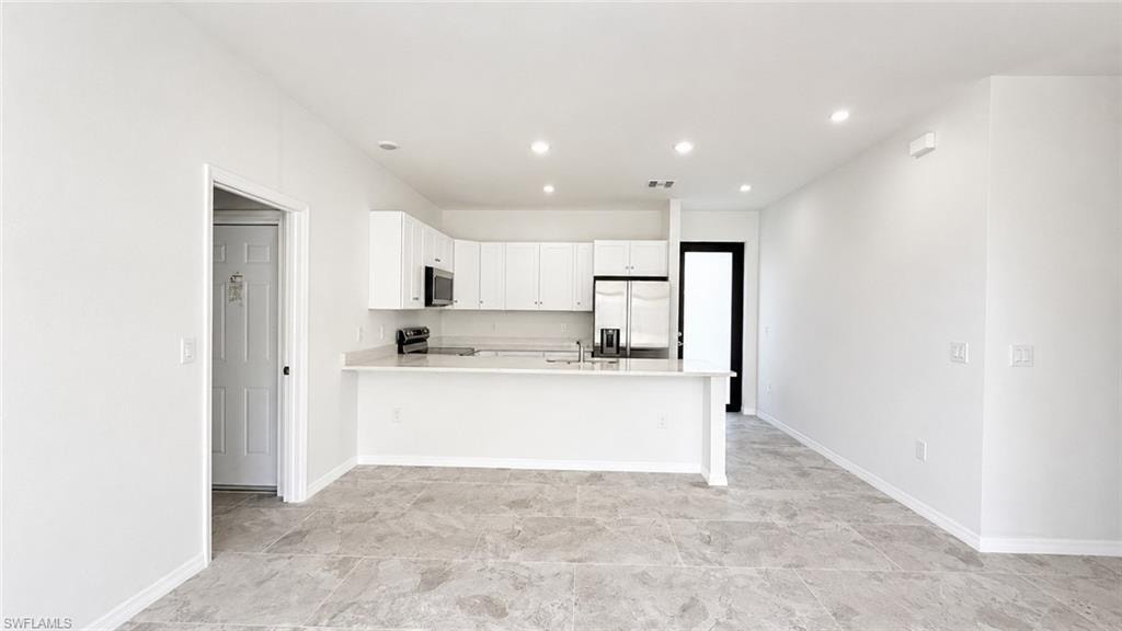 Open-concept living and kitchen area featuring white cabinetry, stainless steel appliances, light-finish countertops, recessed ceiling lighting, and light-hued tile flooring throughout