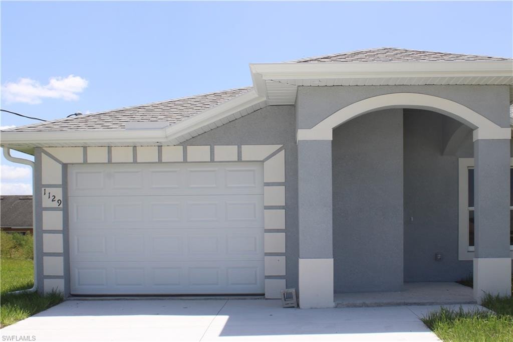 Exterior featuring a light gray stucco finish, white trim accents, arched entryway, and an attached garage with a concrete driveway