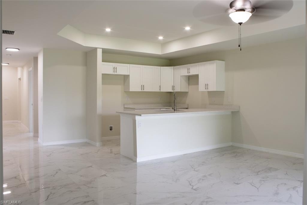 Open-concept area featuring white shaker cabinetry, an integrated sink, light-toned countertops, recessed lighting, and large format polished tile flooring