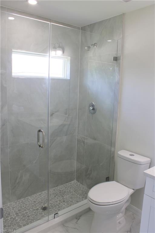 Glass-enclosed shower with gray tiled walls and pebble-finish floor