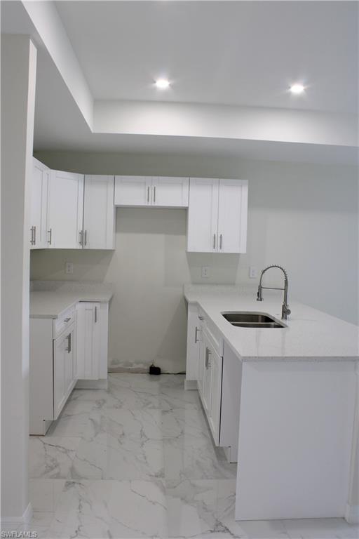 Kitchen featuring white shaker cabinetry, light-toned countertops, a stainless steel sink with pull-down faucet, recessed lighting, and large format floor tiling
