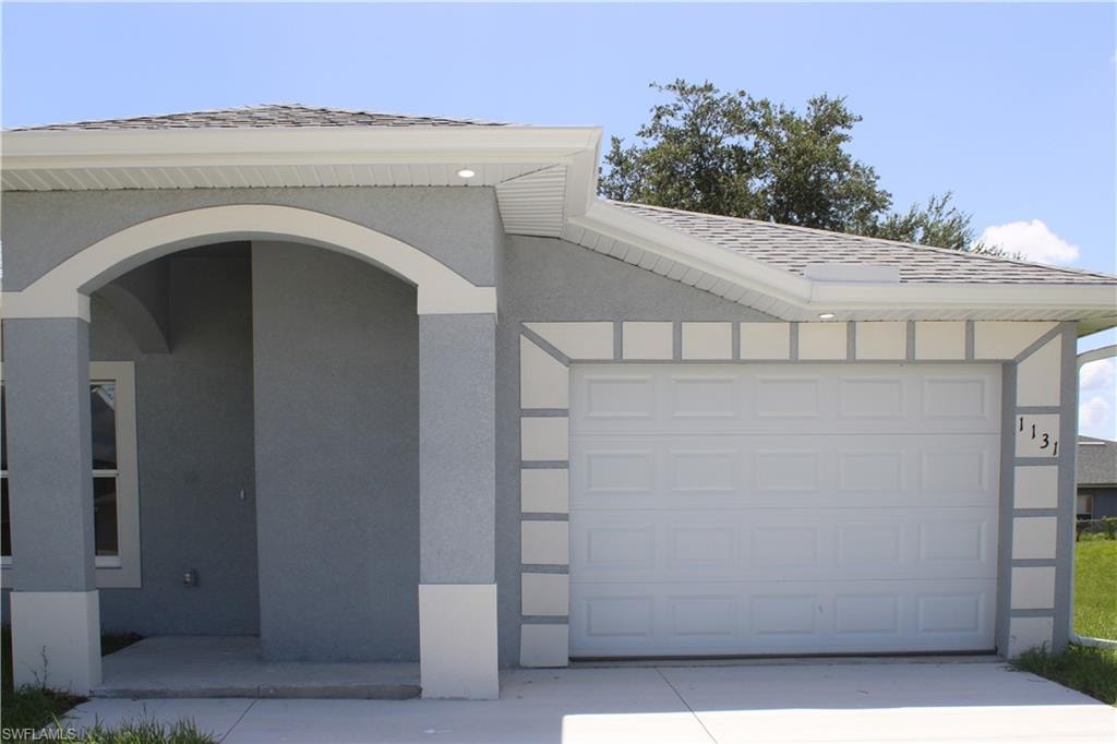 Exterior featuring a light gray stucco finish, white trim accents, arched entryway, and an attached garage with a concrete driveway