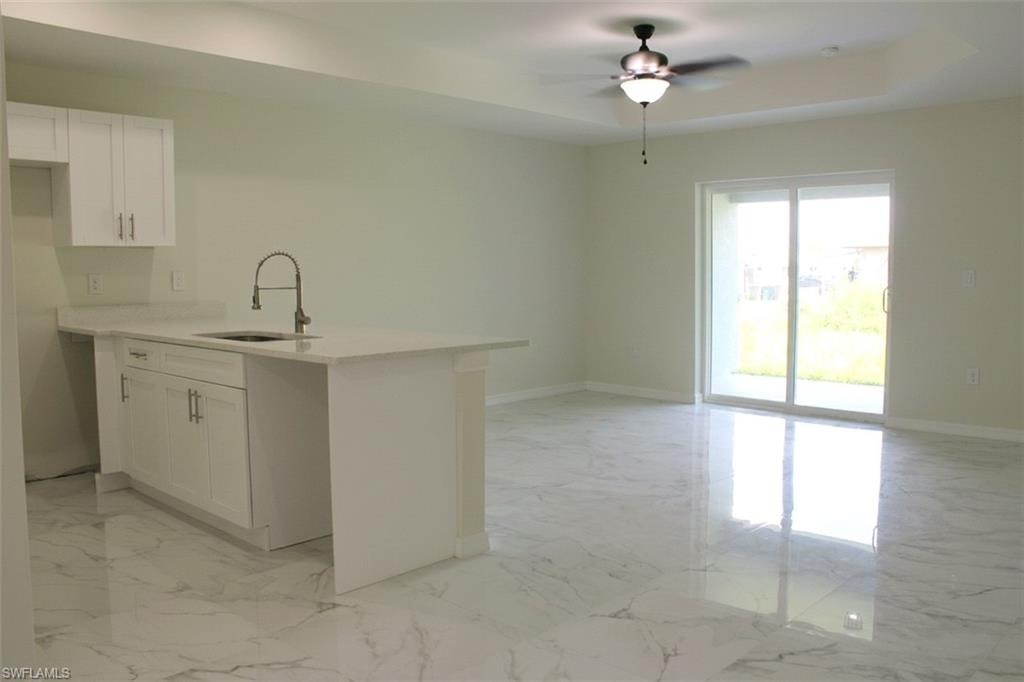 White kitchen cabinetry, light-toned countertops, a kitchen island with an integrated sink, a ceiling fan with light fixture, and sliding glass doors