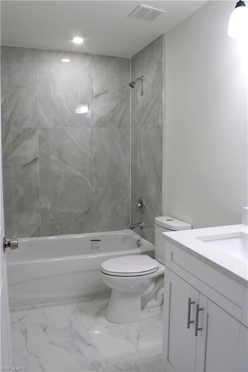 Bathroom featuring a shower/tub combination with gray tile surround, a white vanity with a light-colored countertop, and a white toilet