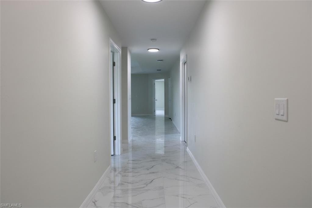 Recessed lighting illuminates the hallway, featuring white walls and polished marble-look tile flooring