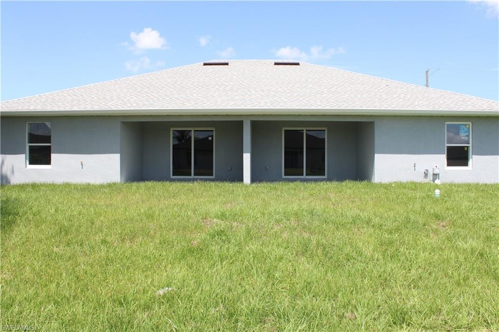 Rear exterior featuring a light gray stucco finish, multiple sliding glass doors, white-framed windows, and a shingled roof