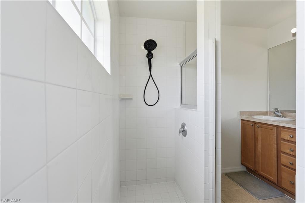 White tiled shower enclosure with a black matte showerhead, handheld sprayer, and built-in shelf