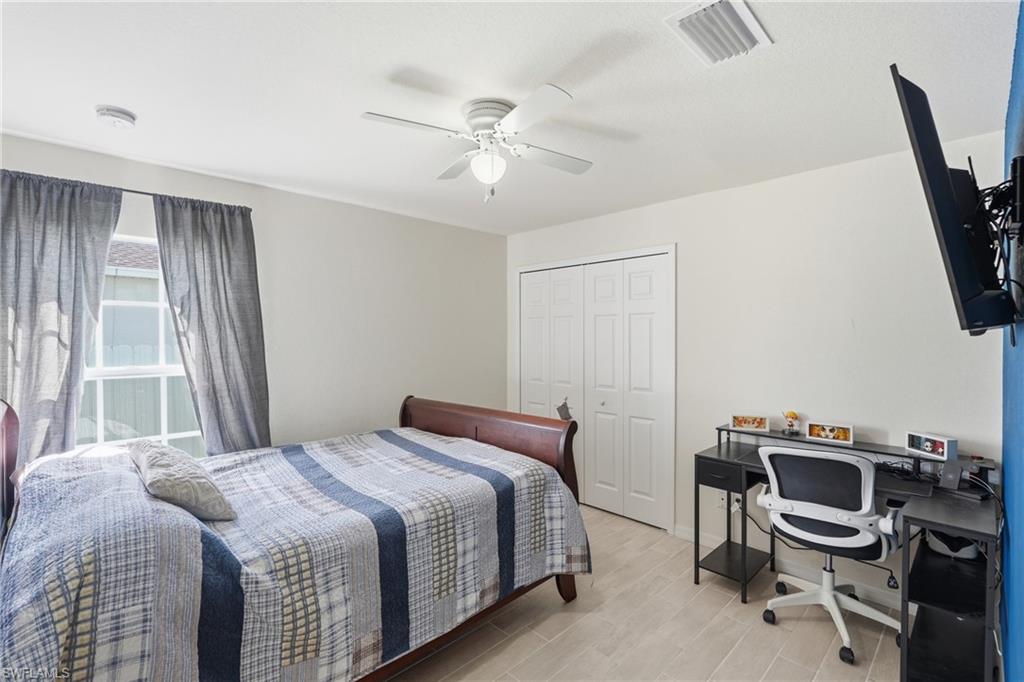 Guest bedroom with light tile flooring, multi-pane window, white bi-fold closet doors, and a ceiling fan with integrated lighting