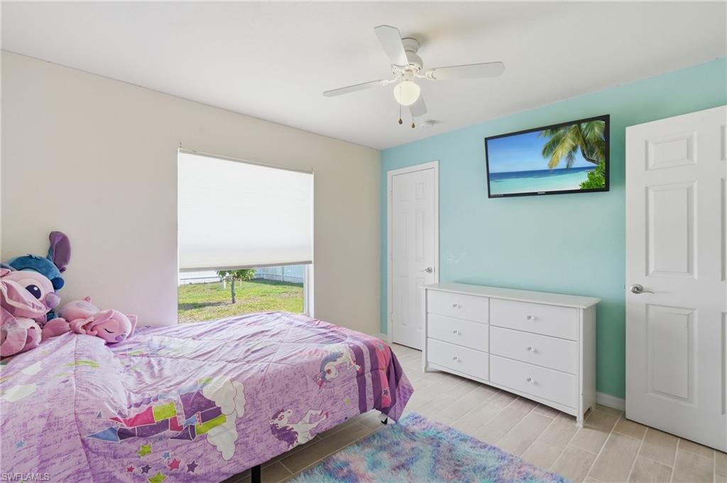 Guest bedroom, natural light from large window, light wood-finish plank tile flooring, and a ceiling fan with integrated lighting