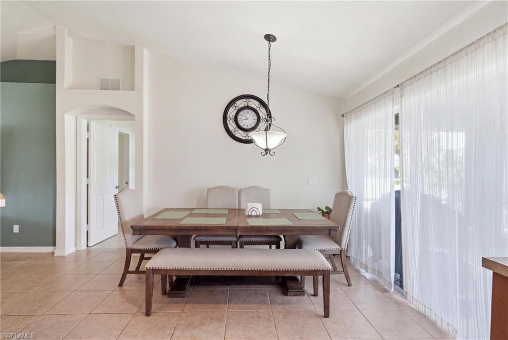 Vaulted ceiling with an attached pendant light fixture, sliding glass doors and tiled flooring