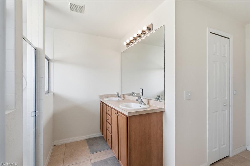 Dual vanity with integrated sinks, wood-finish cabinetry, a large mirror, and overhead strip lighting