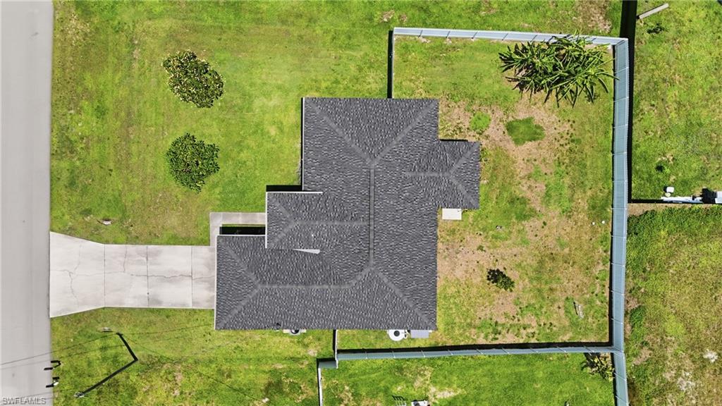 Pitched shingle roof, expansive grassed lot, paved driveway, mature landscaping, and perimeter fencing