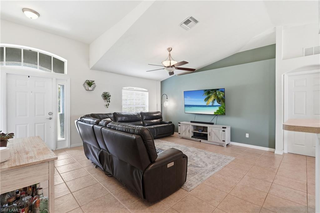 Vaulted ceiling, ceiling fan with integrated lighting, tile flooring, arched transom window, and a single-panel entry door with sidelight