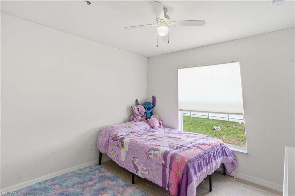 Guest bedroom, natural light from large window, light wood-finish plank tile flooring, and a ceiling fan with integrated lighting