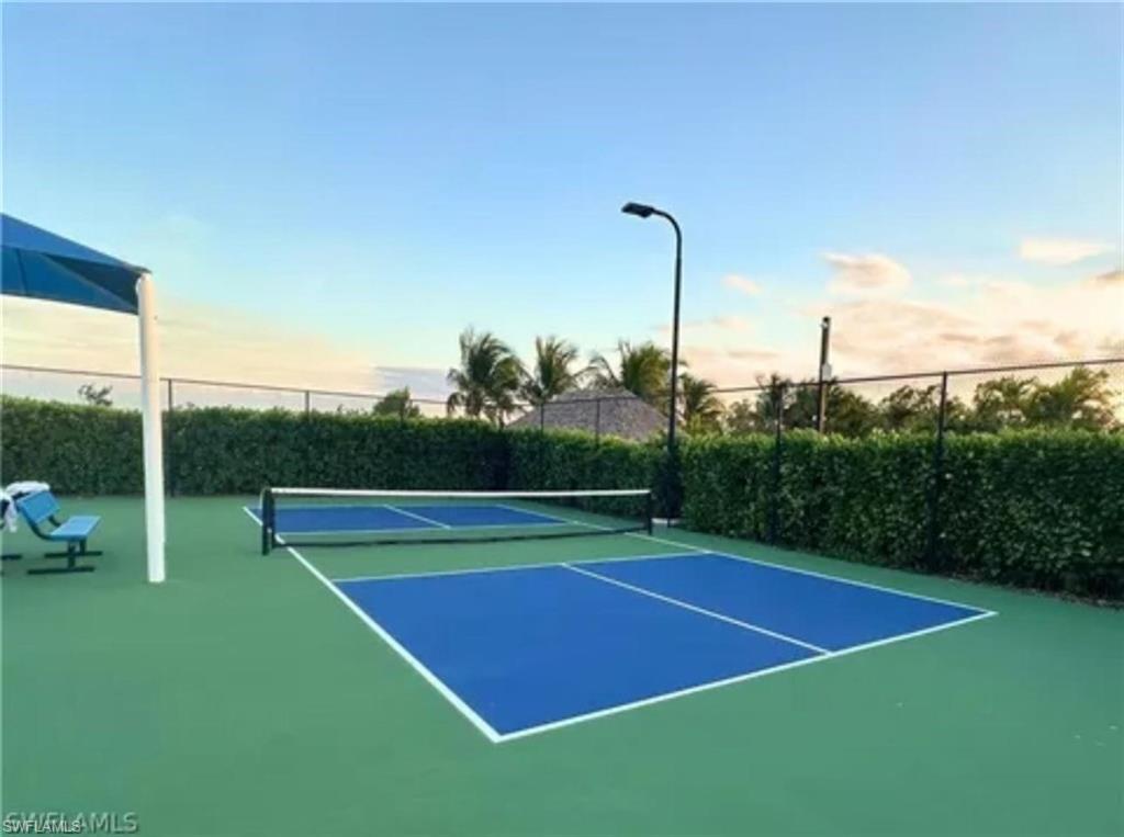 Outdoor pickleball court featuring a green and blue surface, perimeter fencing, and mature landscaping