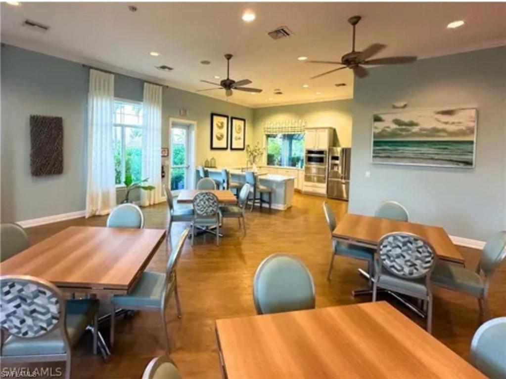 Spacious open-concept dining and kitchen area featuring wood-finish flooring throughout, recessed ceiling lighting, ceiling fans, and large windows with natural light