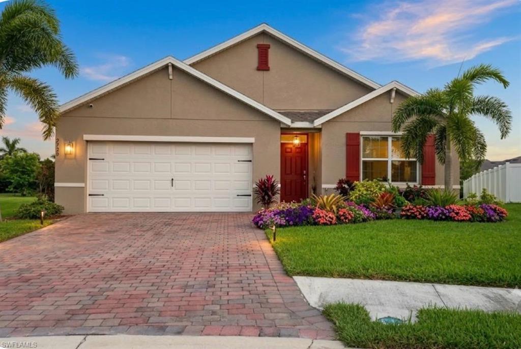 Stucco exterior with a gable roof, paver driveway, an attached two-car garage, and extensive front landscaping