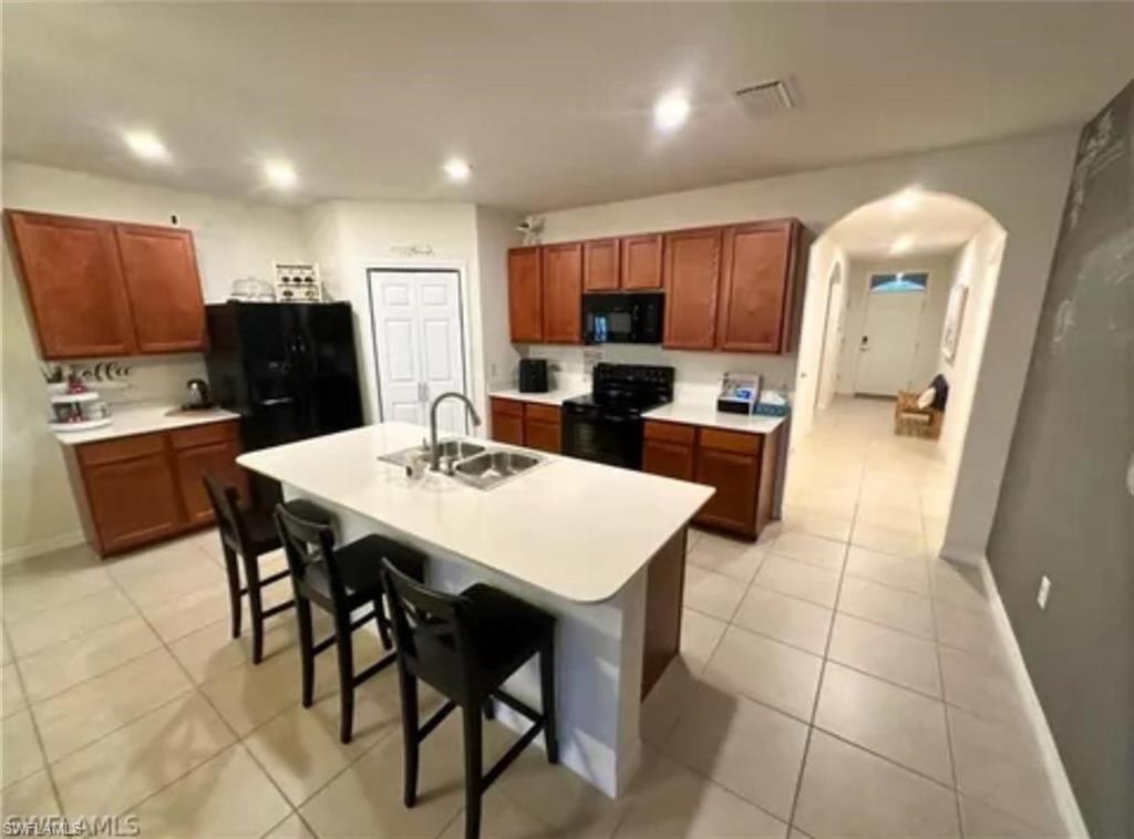 Kitchen featuring a central island with an integrated sink, dark wood-finish cabinetry, and light-toned countertops