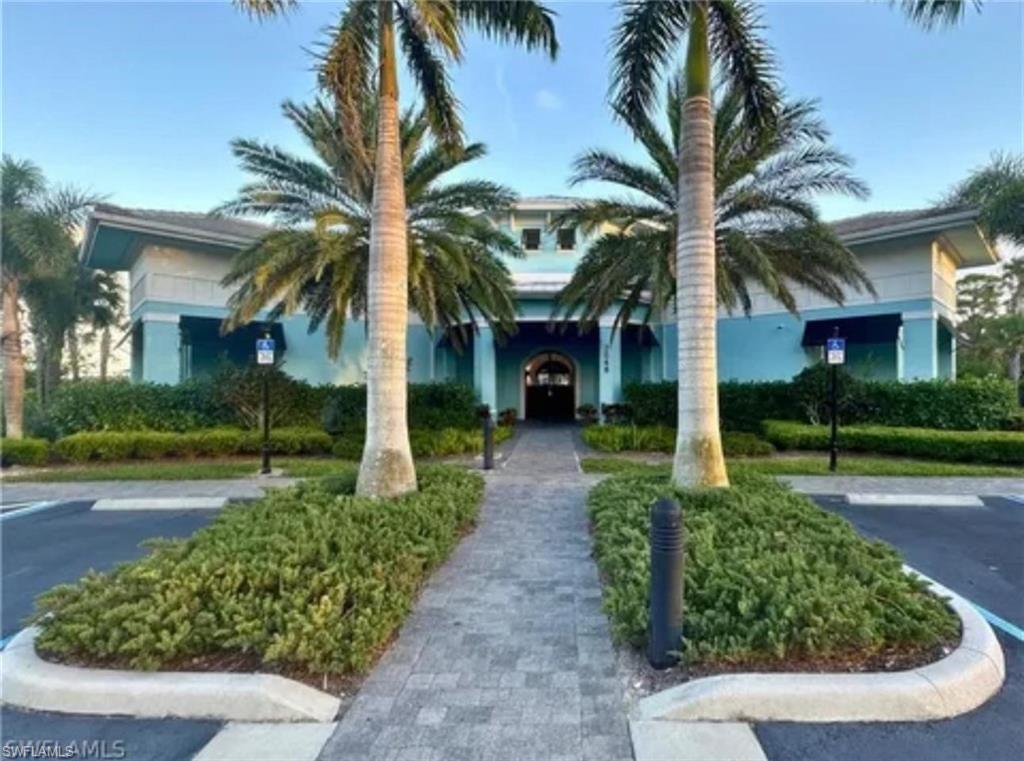 Building with light blue and teal exterior siding, stone paver walkway, mature palm trees, landscaped shrubbery, and parking lot