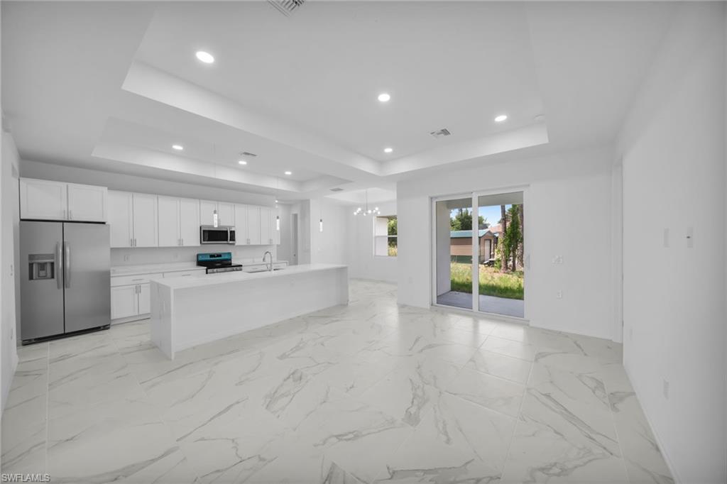 Open-concept kitchen and living area featuring white cabinetry, stainless steel appliances, and a central island