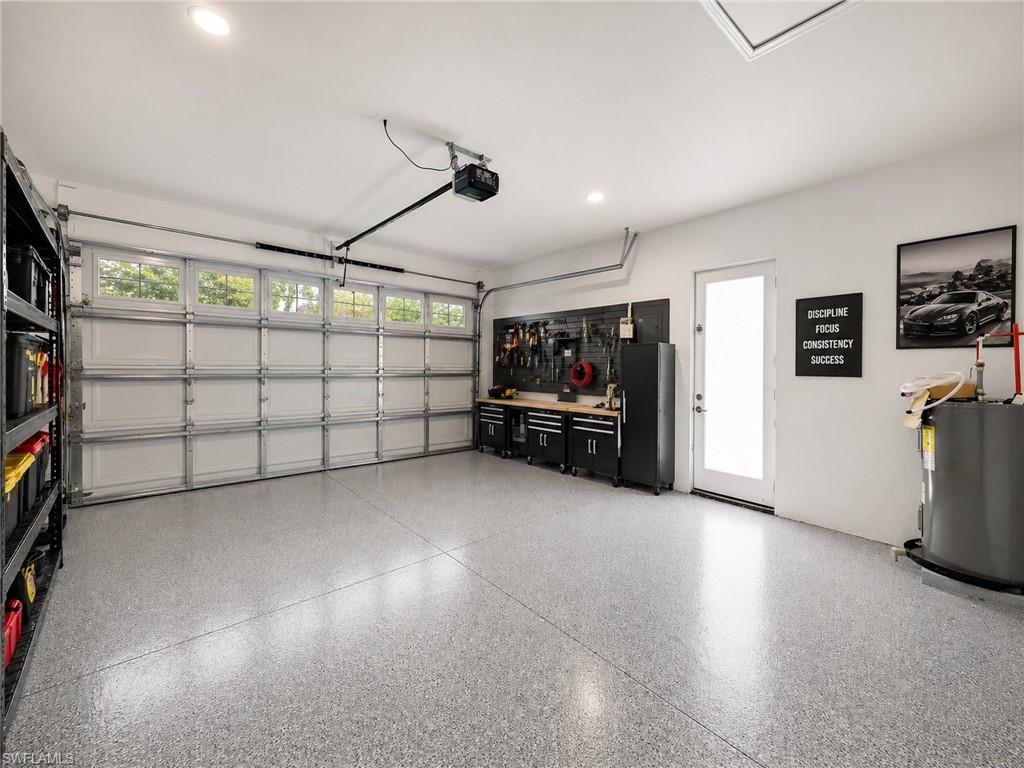 Virtually staged: Spacious garage featuring a speckled epoxy floor coating, paneled garage door with upper window inserts, recessed lighting, and a frosted glass-paneled entry door