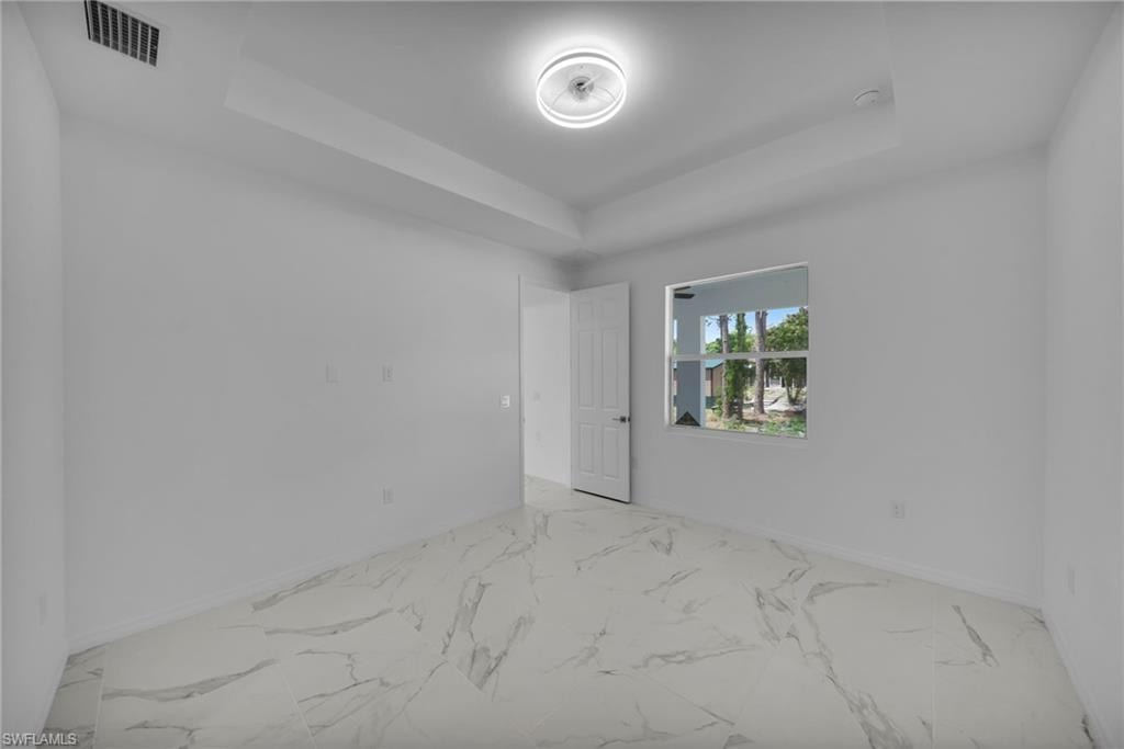 MASTER Spacious interior room featuring large format marble-look tile flooring, white walls, a tray ceiling with a modern flush-mount light fixture, and a window providing natural light