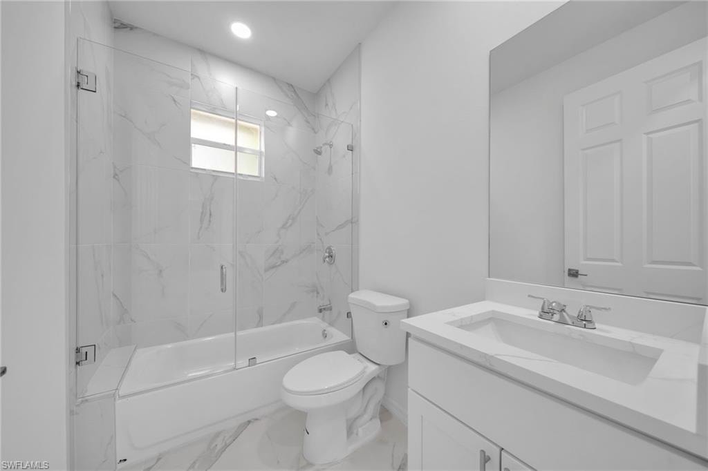 GUEST BATHROOM Bathroom featuring a white bathtub with clear glass shower enclosure, white vanity with integrated sink, and large wall-mounted mirror