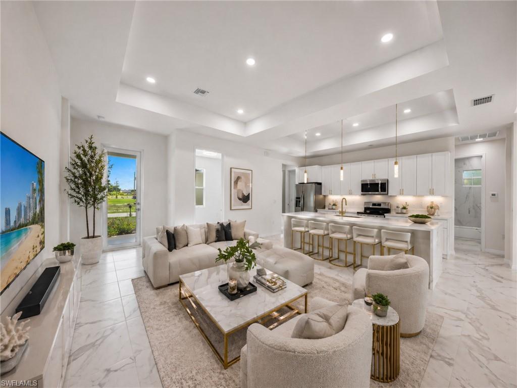 virtually staged: Open-concept interior featuring light-toned large format tile flooring, a tray ceiling with recessed lighting, and a kitchen island with pendant lighting