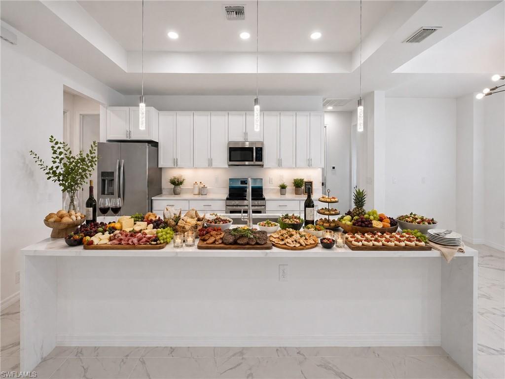 virtually staged:Spacious kitchen featuring a large waterfall island with a light-toned countertop, white cabinetry, integrated stainless steel appliances, and recessed lighting