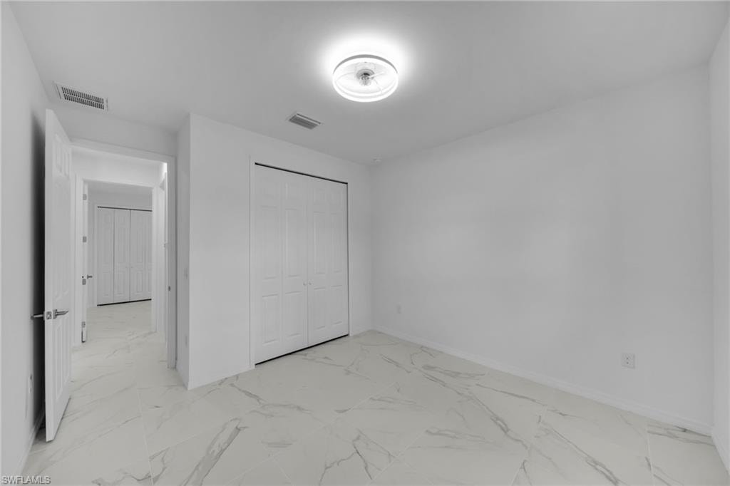 GUEST Room 2 featuring white walls, white bifold closet doors, and white marble-look tile flooring