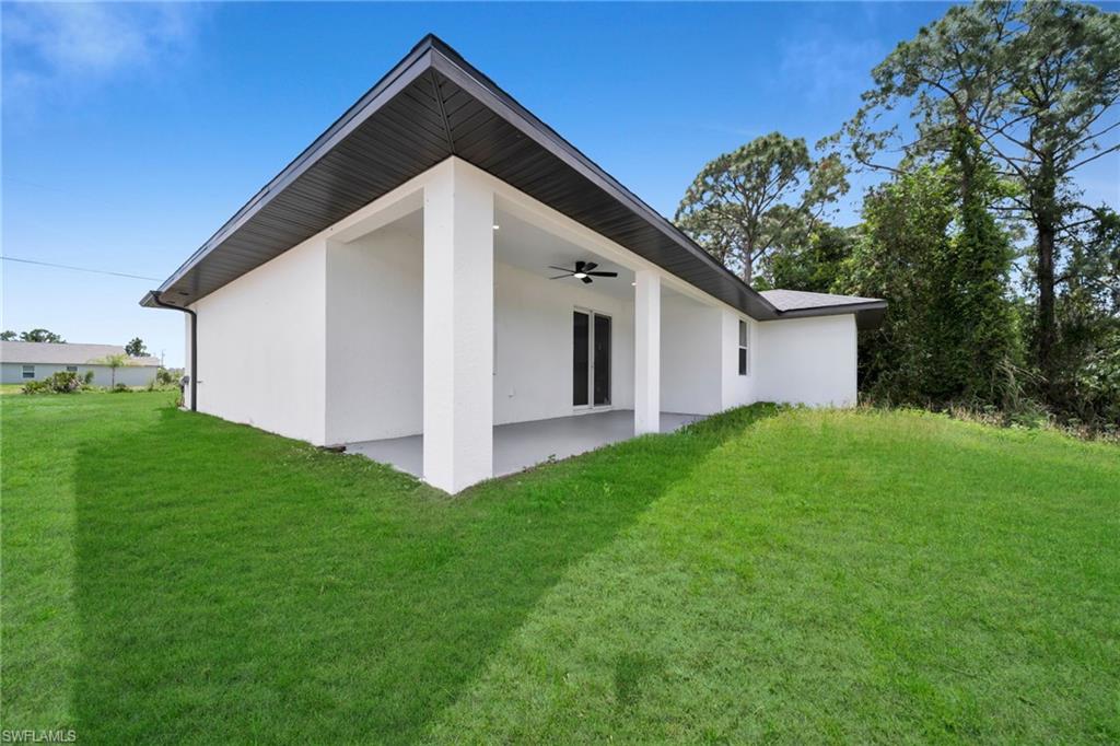 Rear exterior featuring a covered patio with a ceiling fan, white stucco finish, dark roofline, and a lush green lawn (grass color has been enhanced)