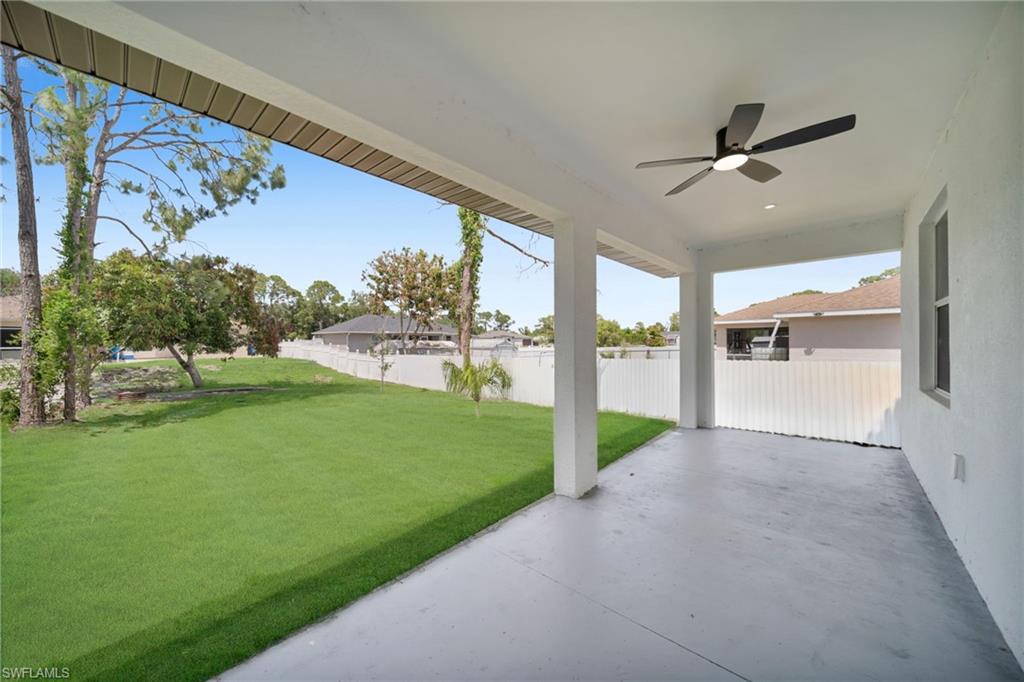 Spacious covered patio with a contemporary ceiling fan, concrete flooring, and multiple support columns (grass color has been enhanced)