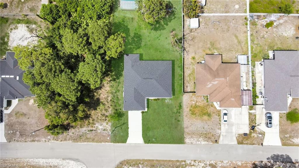 Aerial perspective showcasing a property with a dark shingle roof and a concrete driveway (grass color has been enhanced)